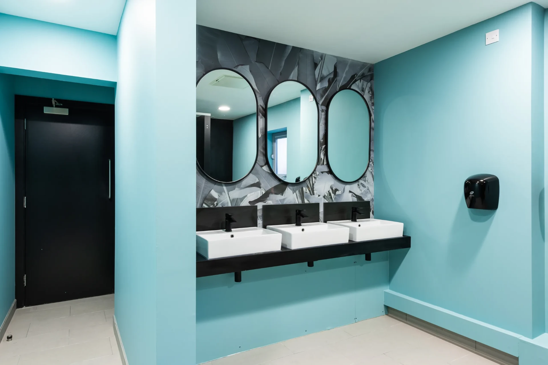 Arden University teal washroom with oval mirrors