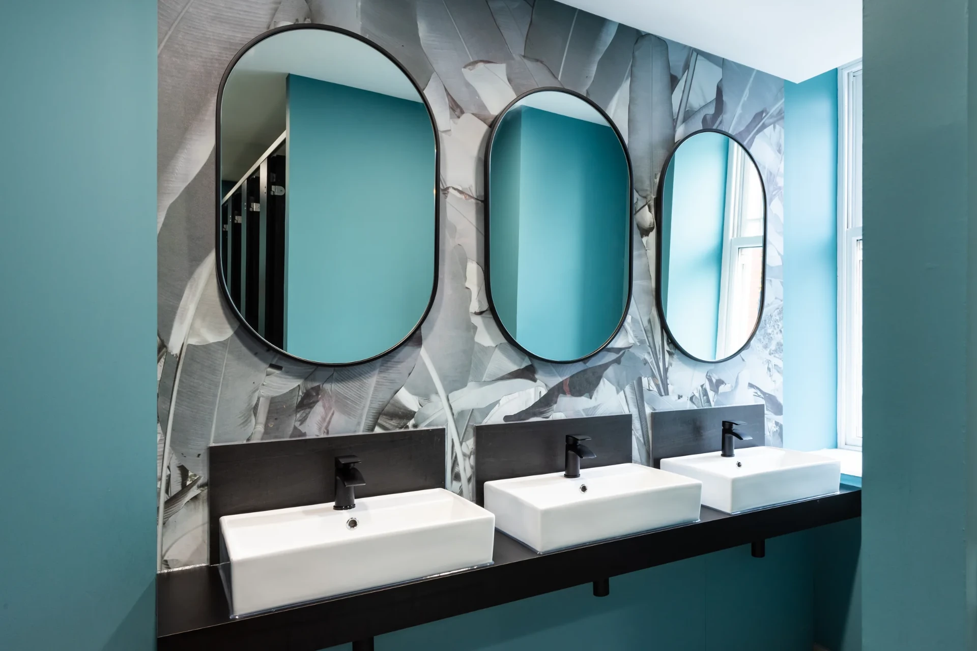 Arden University washroom with teal walls, oval mirrors and patterned feature wall